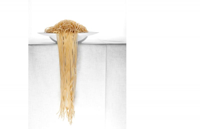 Spaghetti hängen vom Teller herunter. Teller mit Pasta steht auf einem Tisch.
